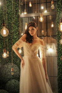 Elevate your special day with our Robe Mae. The elegant column silhouette features stunning beaded lace for a touch of glamour, while the off-shoulder sheer sleeves and deep v-neckline add a hint of romance. Complete the look with the delicate tulle skirt, for a dreamy and unforgettable bridal ensemble.