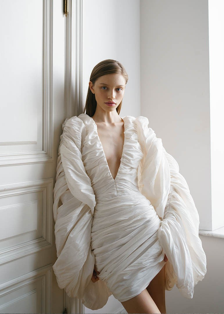 The Venice Mini Dress features a refined, short silhouette complemented by voluminous Venetian sleeves. Crafted entirely from handcrafted crinkled taffeta, it offers a unique texture that enhances its elegant appeal. Perfect for sophisticated occasions, this dress balances statement details with understated charm.