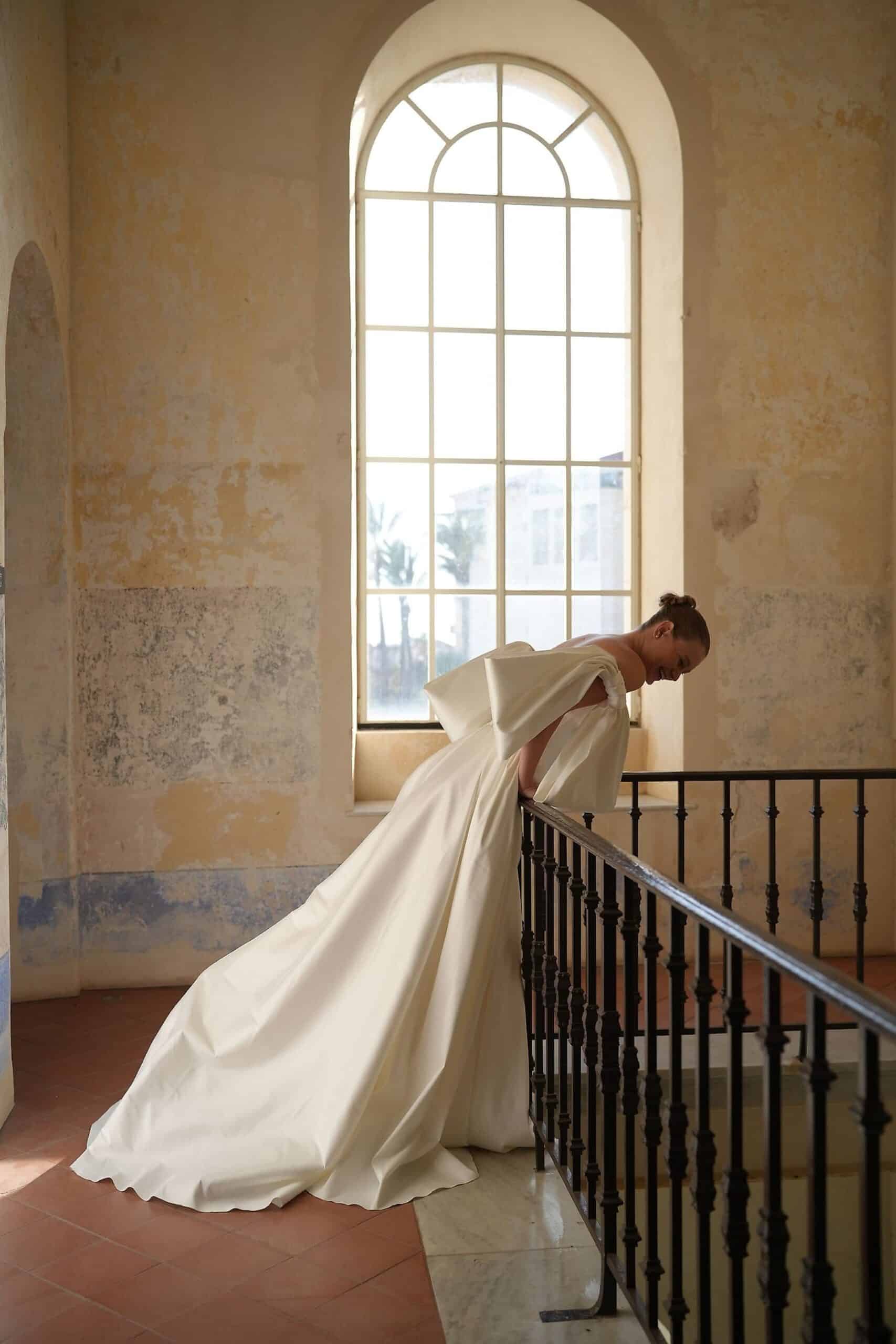 Elevate your special day with the Blue Gown. Made from luxurious Silk Mikado, it features a strapless sweetheart corset and basque waist for a flattering fit. The unique bow-shaped off-shoulder sleeves, coordinating gloves, and matching veil add a touch of elegance and sophistication. Create unforgettable memories in this stunning princess gown.