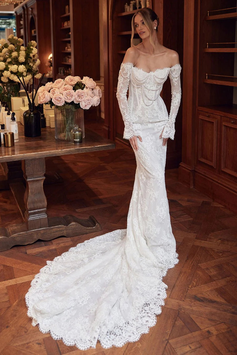 The Caprice Gown exudes royal elegance with its scalloped lace bodice, adorned with pearls and delicate lace sleeves that grace the hands. The unique scalloped detail extends to the hem and train, adding a touch of cascading beauty. Perfect for a regal and sophisticated look on any special occasion.