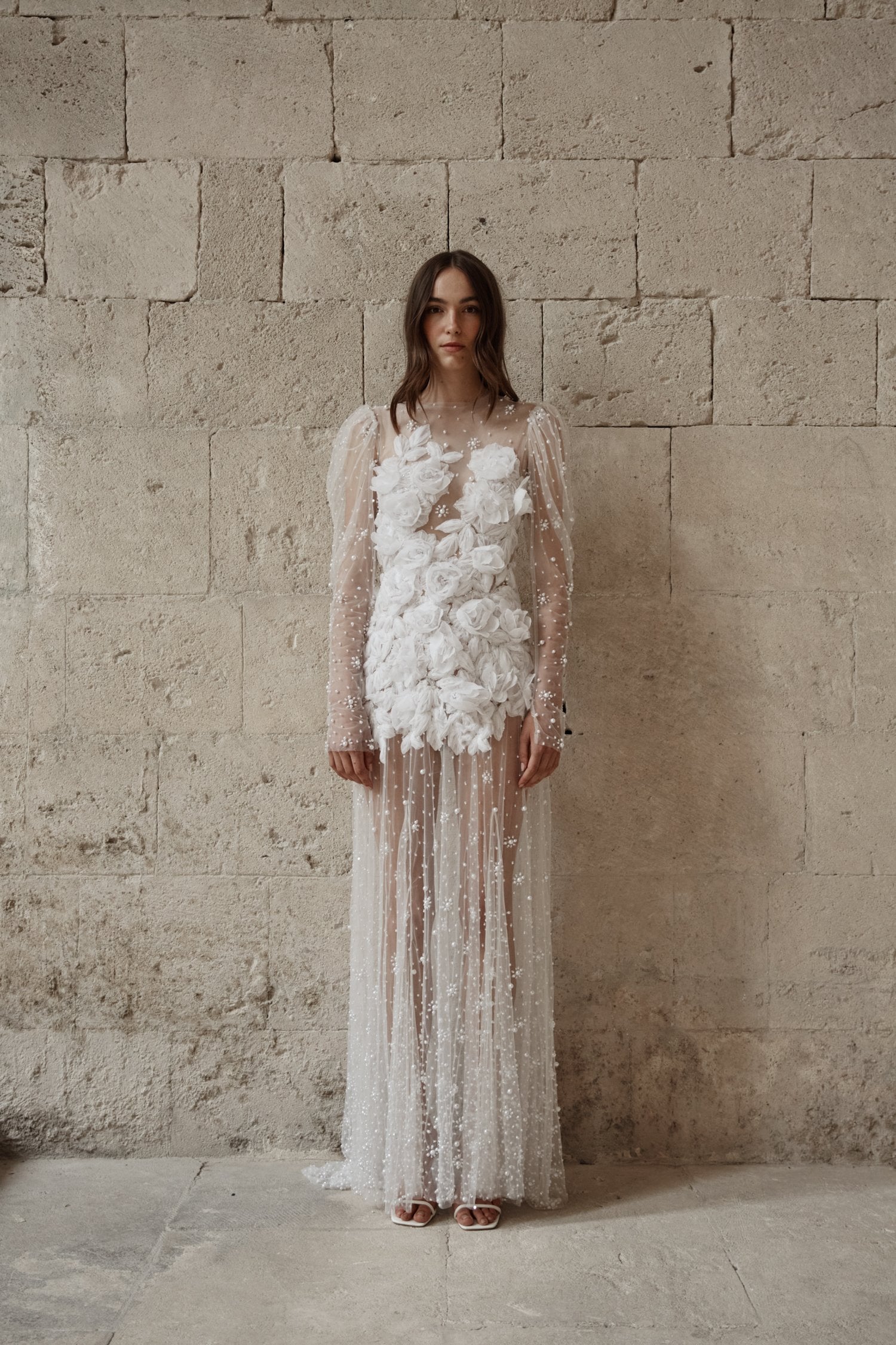 The Scarlett Dress is a dream come true for the romantic bride. Crafted from soft tulle, the bodice is adorned with delicate pearl beading and stunning 3D floral appliques, while the long sleeves and sheer godet skirt add a touch of whimsy and movement. Make a statement on your special day with this magical design.