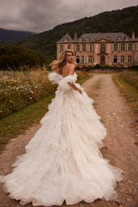 Introducing Dress Esmeralda - a stunning, voluminous dress in a light nude tone with a detachable train. The off-the-shoulder corset is adorned with delicate lace and handmade embroidery, while the flowing sleeves and ruffled bodice add a touch of elegance. The airy skirt is adorned with intricate lace and 3D floral appliques, creating a truly unique and unforgettable look. Perfect for any special occasion.