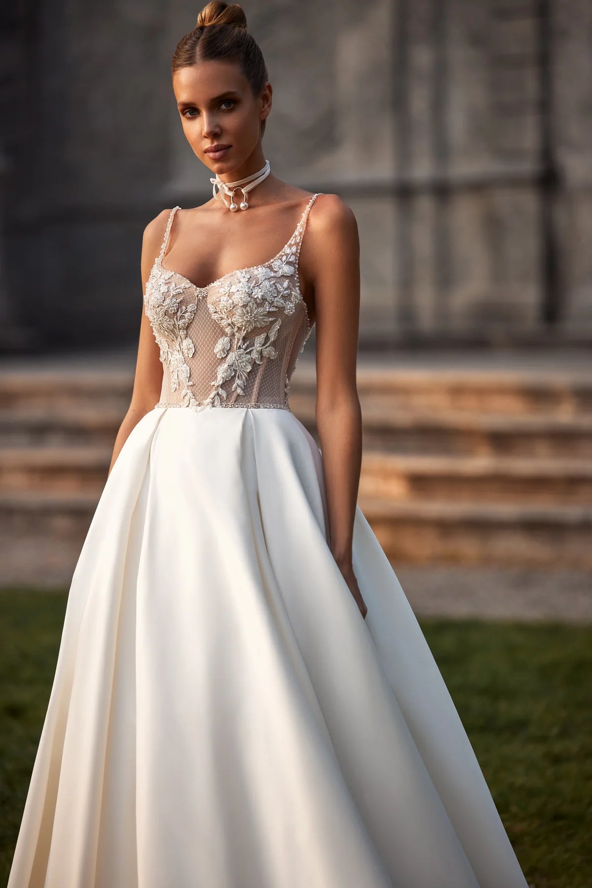 Elevate your special day with the Nelly Gown. This ballgown-style dress features a cinched waist and a dramatic train, while delicate tulle straps, lace flowers, and intricate beading add a touch of romance. The open back and subtle beaded belt add a modern twist to this traditional design. The full satin skirt is adorned with stunning lace details for a look that exudes elegance and grace.