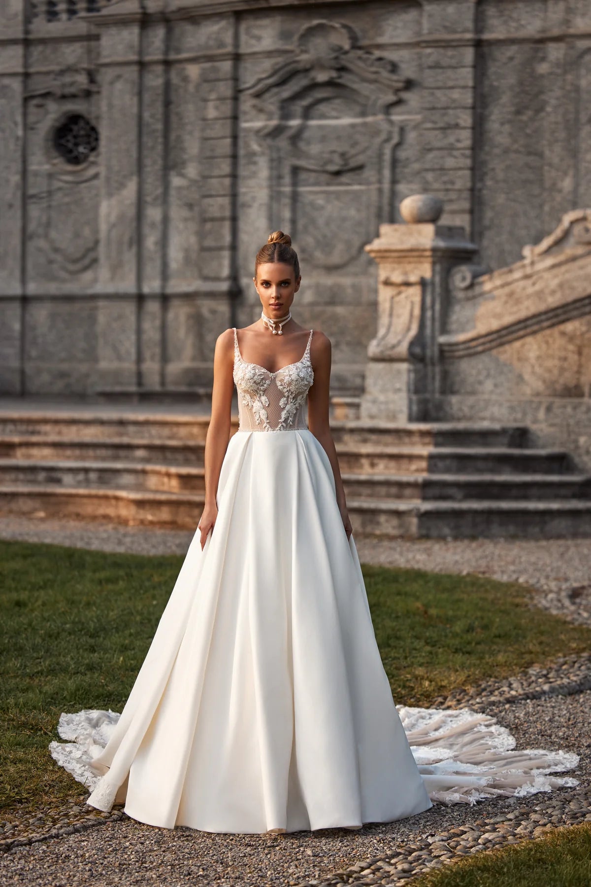 Elevate your special day with the Nelly Gown. This ballgown-style dress features a cinched waist and a dramatic train, while delicate tulle straps, lace flowers, and intricate beading add a touch of romance. The open back and subtle beaded belt add a modern twist to this traditional design. The full satin skirt is adorned with stunning lace details for a look that exudes elegance and grace.