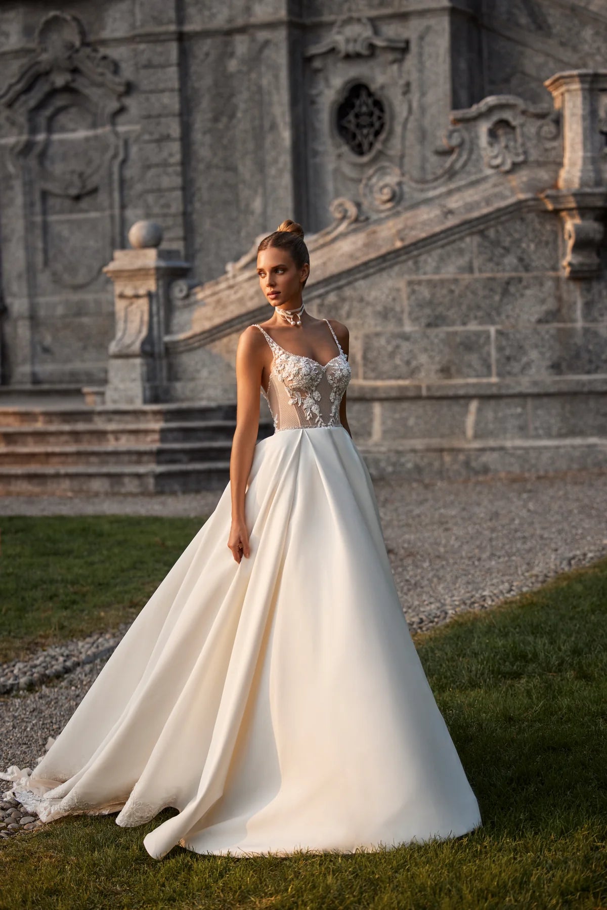 Elevate your special day with the Nelly Gown. This ballgown-style dress features a cinched waist and a dramatic train, while delicate tulle straps, lace flowers, and intricate beading add a touch of romance. The open back and subtle beaded belt add a modern twist to this traditional design. The full satin skirt is adorned with stunning lace details for a look that exudes elegance and grace.