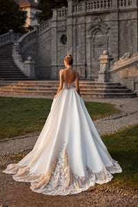 Elevate your special day with the Nelly Gown. This ballgown-style dress features a cinched waist and a dramatic train, while delicate tulle straps, lace flowers, and intricate beading add a touch of romance. The open back and subtle beaded belt add a modern twist to this traditional design. The full satin skirt is adorned with stunning lace details for a look that exudes elegance and grace.