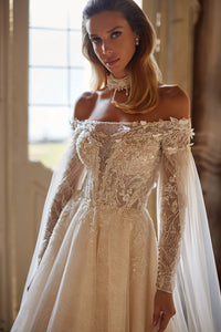 Experience ethereal elegance in the Anastasia Gown. Hand-embroidered with delicate lace, sequins, beads, pearls, 3D flowers, and butterflies, this nude a-line dress features an off-shoulder bodice with long sleeves and a hidden zipper closure. The airy mesh inserts on the sleeves and pleated skirt add a whimsical touch.