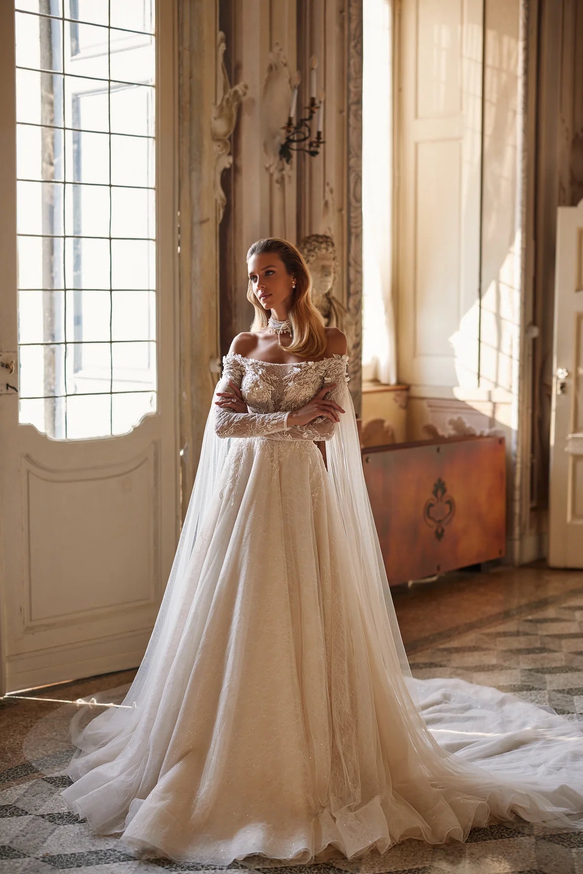 Experience ethereal elegance in the Anastasia Gown. Hand-embroidered with delicate lace, sequins, beads, pearls, 3D flowers, and butterflies, this nude a-line dress features an off-shoulder bodice with long sleeves and a hidden zipper closure. The airy mesh inserts on the sleeves and pleated skirt add a whimsical touch.