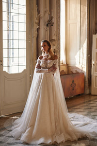 Experience ethereal elegance in the Anastasia Gown. Hand-embroidered with delicate lace, sequins, beads, pearls, 3D flowers, and butterflies, this nude a-line dress features an off-shoulder bodice with long sleeves and a hidden zipper closure. The airy mesh inserts on the sleeves and pleated skirt add a whimsical touch.