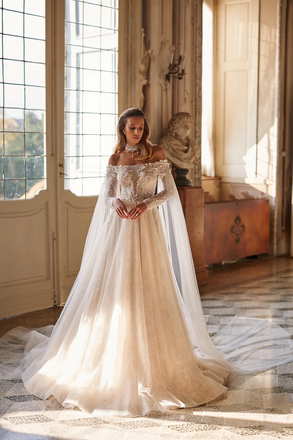 Experience ethereal elegance in the Anastasia Gown. Hand-embroidered with delicate lace, sequins, beads, pearls, 3D flowers, and butterflies, this nude a-line dress features an off-shoulder bodice with long sleeves and a hidden zipper closure. The airy mesh inserts on the sleeves and pleated skirt add a whimsical touch.