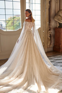 Experience ethereal elegance in the Anastasia Gown. Hand-embroidered with delicate lace, sequins, beads, pearls, 3D flowers, and butterflies, this nude a-line dress features an off-shoulder bodice with long sleeves and a hidden zipper closure. The airy mesh inserts on the sleeves and pleated skirt add a whimsical touch.