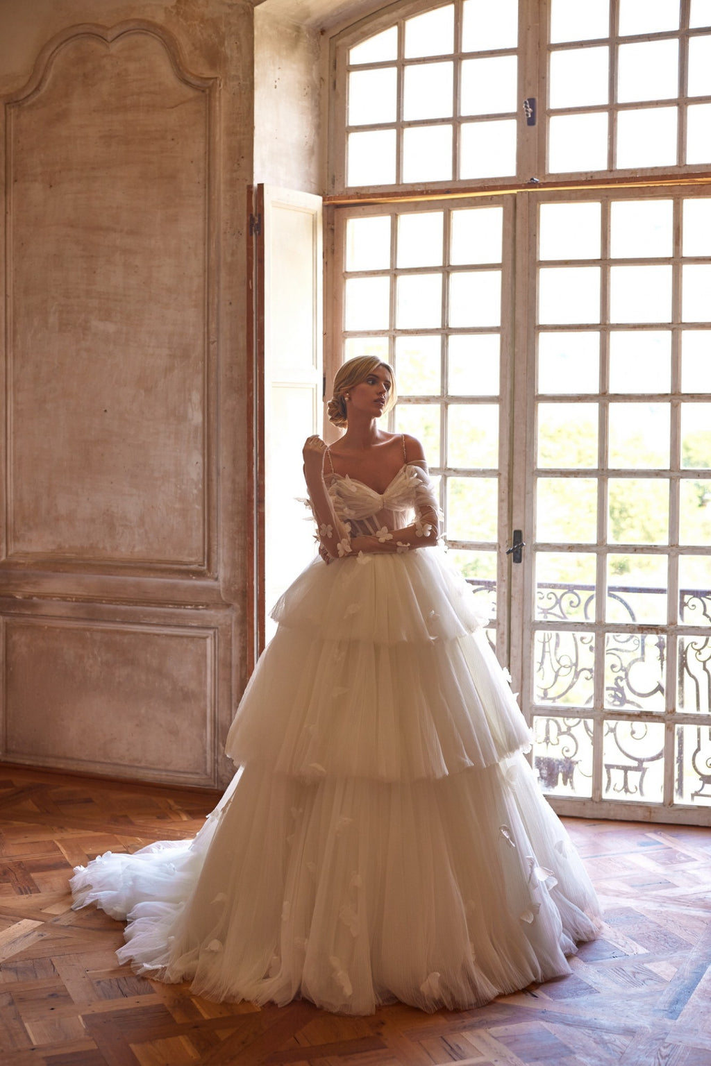 Experience a fairytale in our butterfly dress! Handmade 3D organza butterflies adorn the delicate pleated mesh, while a removable cup corset and embroidered skirt add romance. With off-shoulder straps and a hidden zipper, it's a playful take on the classic ball gown. Complete the look with embellished mesh gloves and a veil, both adorned with handmade butterfly and embroidery details.