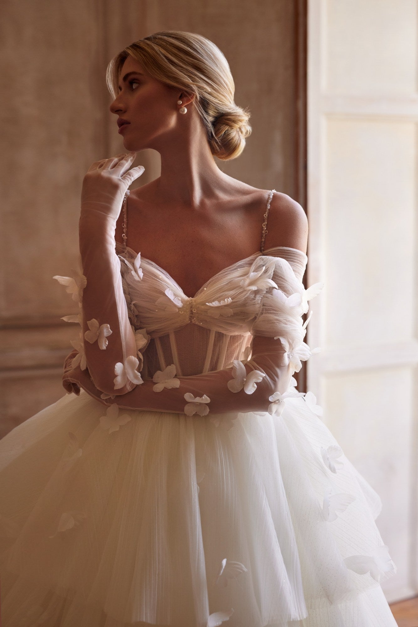 Experience a fairytale in our butterfly dress! Handmade 3D organza butterflies adorn the delicate pleated mesh, while a removable cup corset and embroidered skirt add romance. With off-shoulder straps and a hidden zipper, it's a playful take on the classic ball gown. Complete the look with embellished mesh gloves and a veil, both adorned with handmade butterfly and embroidery details.