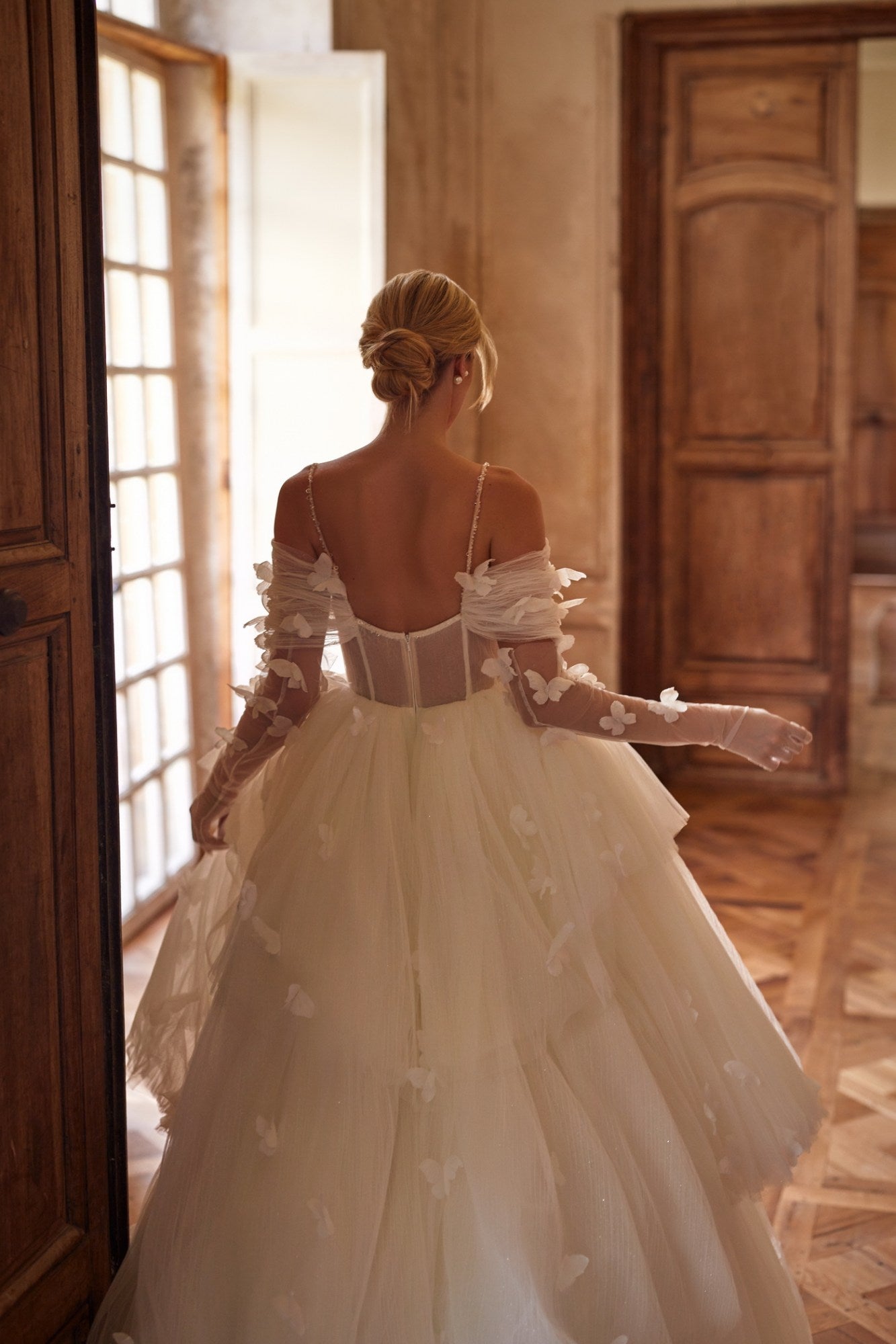 Experience a fairytale in our butterfly dress! Handmade 3D organza butterflies adorn the delicate pleated mesh, while a removable cup corset and embroidered skirt add romance. With off-shoulder straps and a hidden zipper, it's a playful take on the classic ball gown. Complete the look with embellished mesh gloves and a veil, both adorned with handmade butterfly and embroidery details.