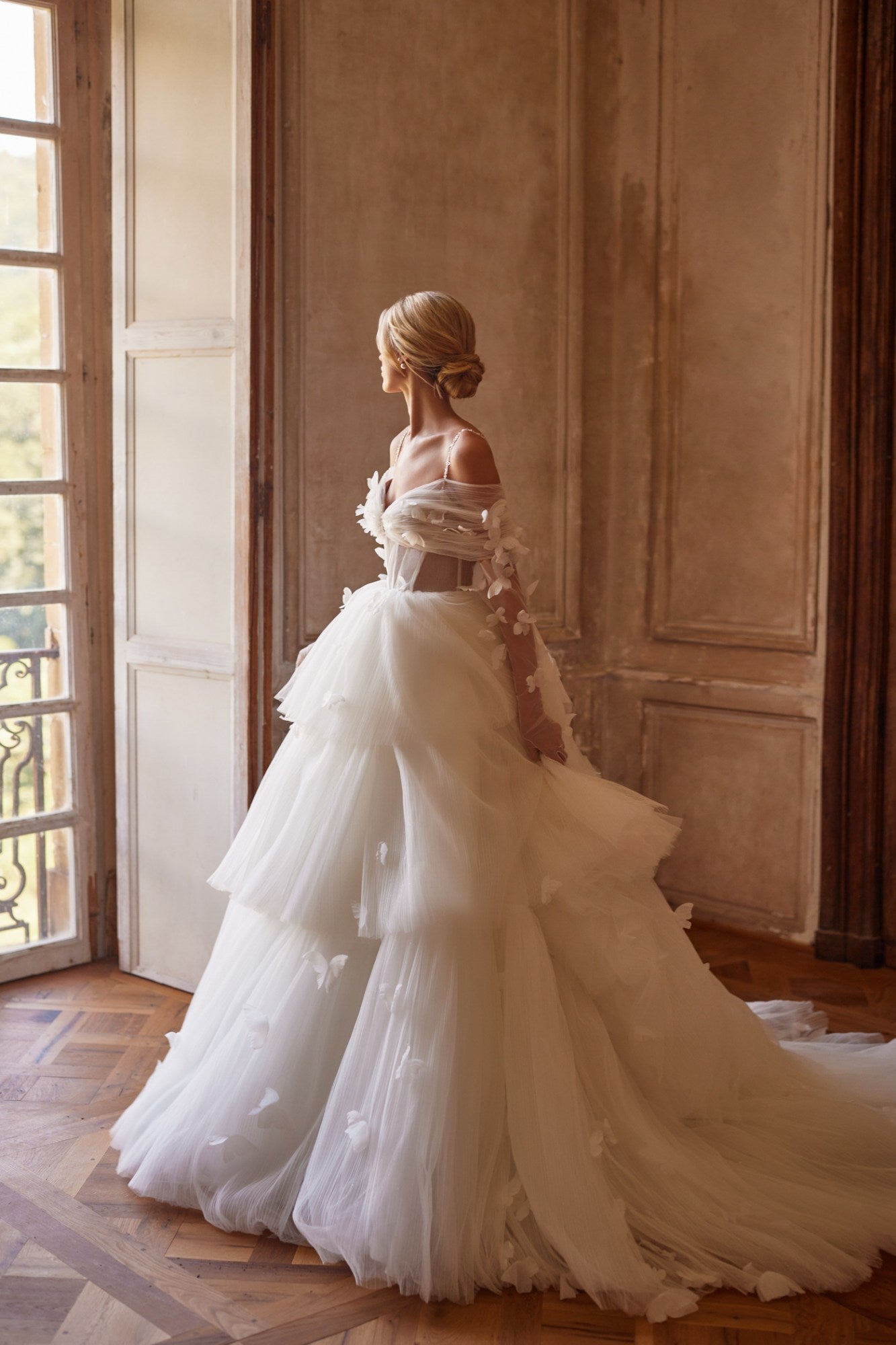 Experience a fairytale in our butterfly dress! Handmade 3D organza butterflies adorn the delicate pleated mesh, while a removable cup corset and embroidered skirt add romance. With off-shoulder straps and a hidden zipper, it's a playful take on the classic ball gown. Complete the look with embellished mesh gloves and a veil, both adorned with handmade butterfly and embroidery details.