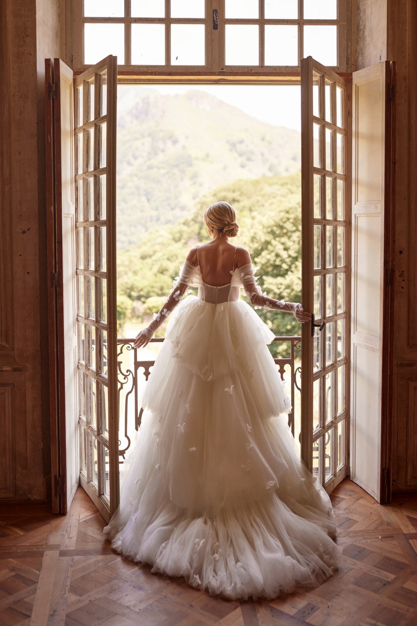Experience a fairytale in our butterfly dress! Handmade 3D organza butterflies adorn the delicate pleated mesh, while a removable cup corset and embroidered skirt add romance. With off-shoulder straps and a hidden zipper, it's a playful take on the classic ball gown. Complete the look with embellished mesh gloves and a veil, both adorned with handmade butterfly and embroidery details.