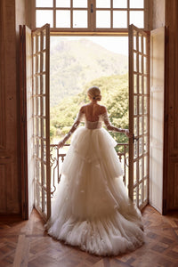Experience a fairytale in our butterfly dress! Handmade 3D organza butterflies adorn the delicate pleated mesh, while a removable cup corset and embroidered skirt add romance. With off-shoulder straps and a hidden zipper, it's a playful take on the classic ball gown. Complete the look with embellished mesh gloves and a veil, both adorned with handmade butterfly and embroidery details.