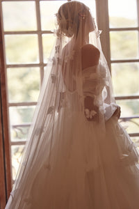 Experience a fairytale in our butterfly dress! Handmade 3D organza butterflies adorn the delicate pleated mesh, while a removable cup corset and embroidered skirt add romance. With off-shoulder straps and a hidden zipper, it's a playful take on the classic ball gown. Complete the look with embellished mesh gloves and a veil, both adorned with handmade butterfly and embroidery details.