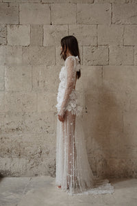 The Scarlett Dress is a dream come true for the romantic bride. Crafted from soft tulle, the bodice is adorned with delicate pearl beading and stunning 3D floral appliques, while the long sleeves and sheer godet skirt add a touch of whimsy and movement. Make a statement on your special day with this magical design.