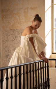 Elevate your special day with the Blue Gown. Made from luxurious Silk Mikado, it features a strapless sweetheart corset and basque waist for a flattering fit. The unique bow-shaped off-shoulder sleeves, coordinating gloves, and matching veil add a touch of elegance and sophistication. Create unforgettable memories in this stunning princess gown.