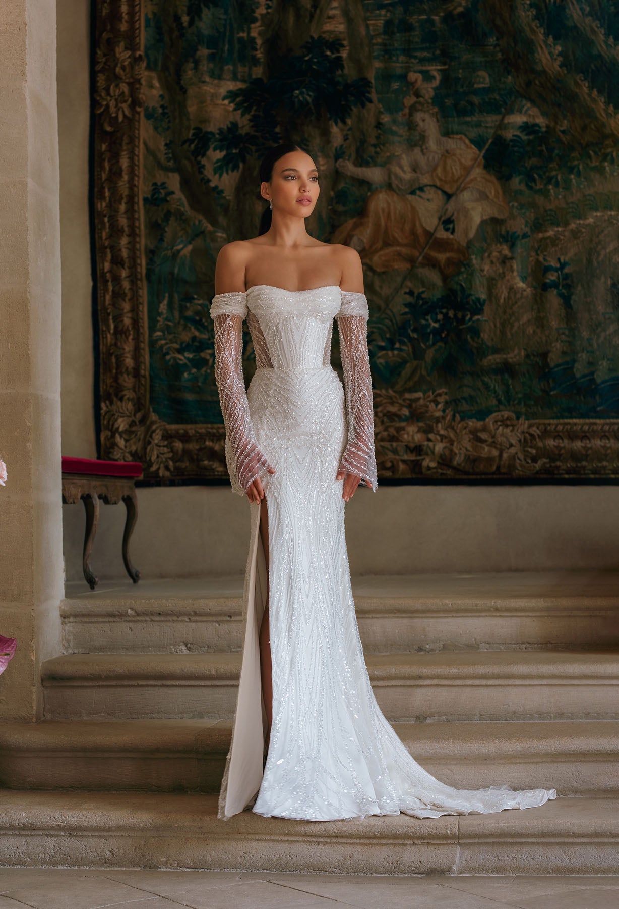Effie is a luxurious fitted mermaid gown made of exclusive beaded lace. The off-shoulder neckline bares the collarbones adding seductiveness, the corset is decorated with sheer nude side pannels and long translucent lace sleeves look extravagant. The sheath skirt is embellished with thigh high slit and a Tulle overskirt is fastened on the waistline.