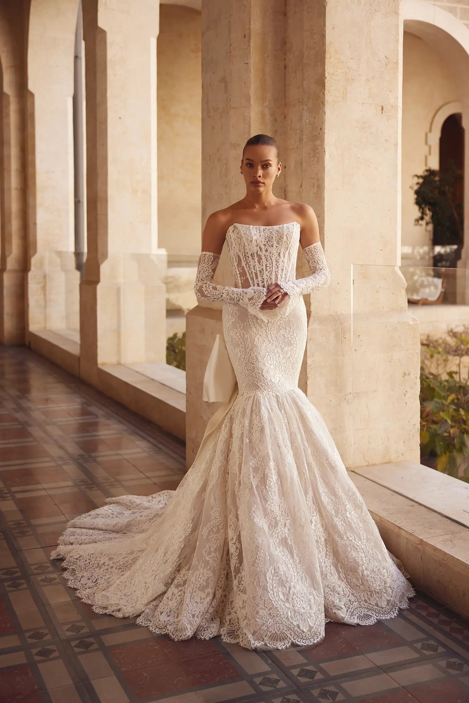 Feel like a true princess in our Melody Gown. The Alençon lace mermaid design and strapless scoop neckline will accentuate your figure, while the signature satin Pnina bow adds a touch of elegance. Complete your look with the coordinating lace bolero and matching gloves for the perfect fairytale wedding.