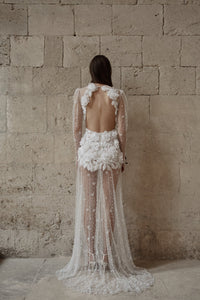 The Scarlett Dress is a dream come true for the romantic bride. Crafted from soft tulle, the bodice is adorned with delicate pearl beading and stunning 3D floral appliques, while the long sleeves and sheer godet skirt add a touch of whimsy and movement. Make a statement on your special day with this magical design.