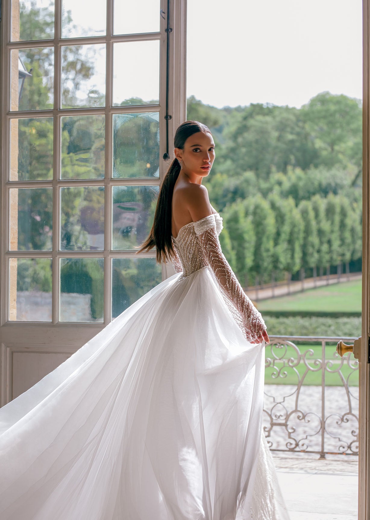 Effie is a luxurious fitted mermaid gown made of exclusive beaded lace. The off-shoulder neckline bares the collarbones adding seductiveness, the corset is decorated with sheer nude side pannels and long translucent lace sleeves look extravagant. The sheath skirt is embellished with thigh high slit and a Tulle overskirt is fastened on the waistline.