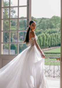 Effie is a luxurious fitted mermaid gown made of exclusive beaded lace. The off-shoulder neckline bares the collarbones adding seductiveness, the corset is decorated with sheer nude side pannels and long translucent lace sleeves look extravagant. The sheath skirt is embellished with thigh high slit and a Tulle overskirt is fastened on the waistline.