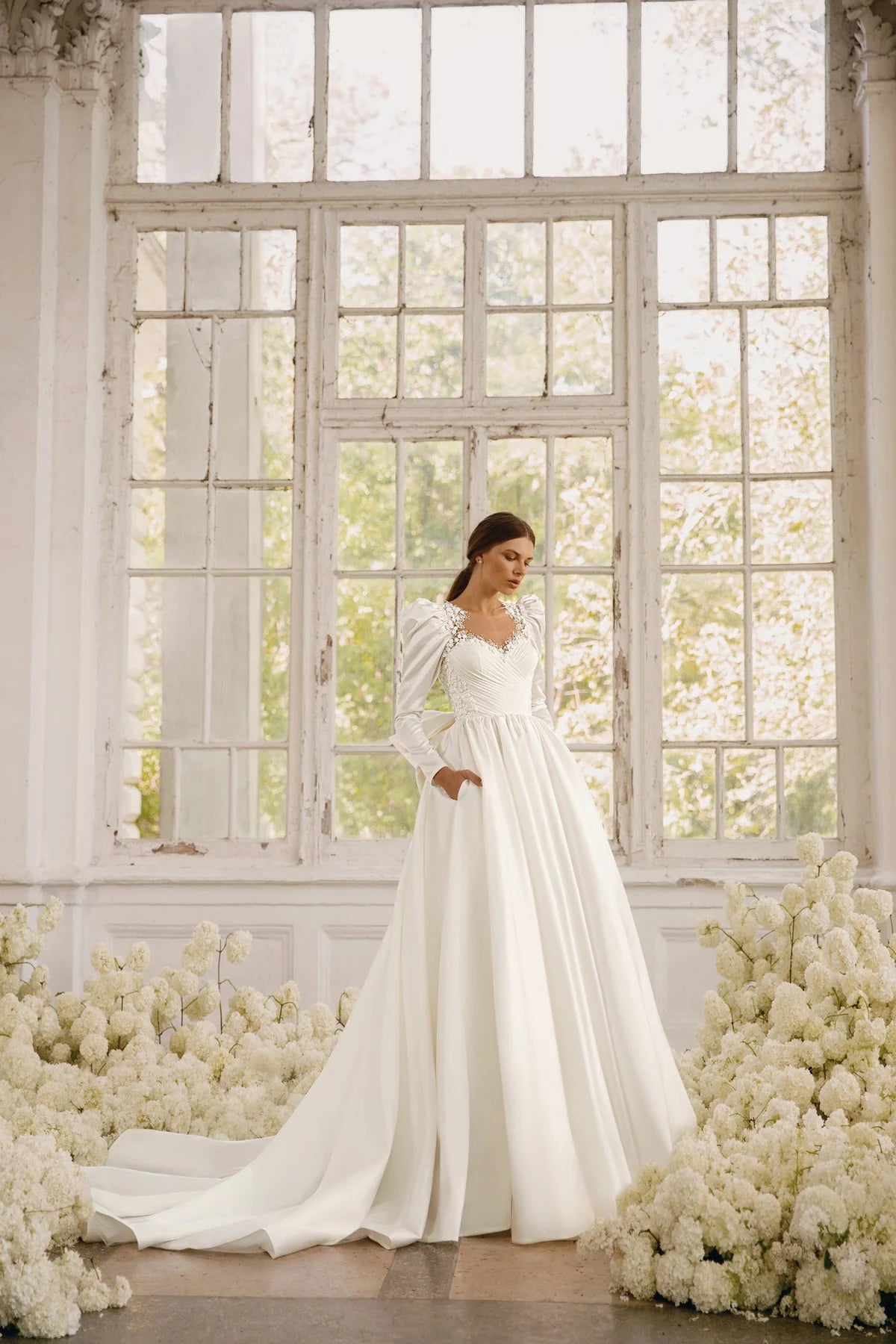 The Rosalee Gown is a breathtaking A-line wedding dress made of luxurious silk satin. The stunning corset features a unique draped design and voluminous puffed sleeves, while delicate hand-embroidered lace adorns the neckline and waistline. With hidden pockets and a removable sash, this dress effortlessly combines elegance and practicality.