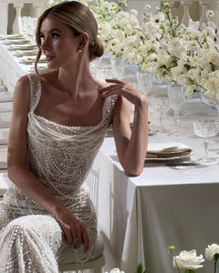 Get ready to dazzle on your special day with the Versy Gown. The fitted silhouette is enhanced by a relief corset made of transparent mesh and lace, adorned with asymmetrical pearl threads. The whimsical silhouette skirt features scattered pearl threads and removable stars for a unique, ethereal touch. Say "I do" in style with the Versy Gown.