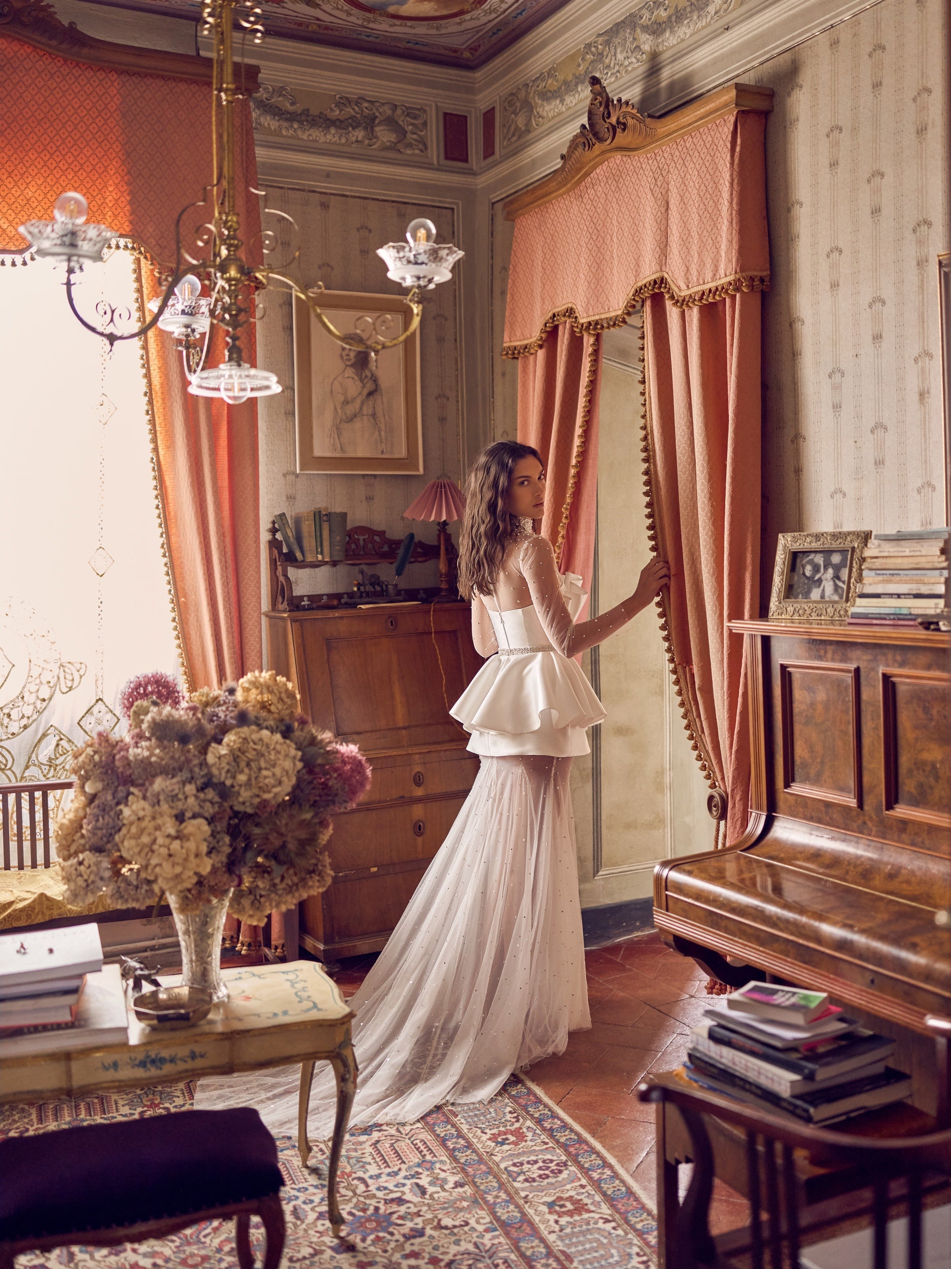 The Cassiopeia Gown captivates with its extraordinary seashell-inspired silhouette and radiant shimmer. Crafted from glossy mikado and crystal-embellished tulle, it features a neckline richly detailed with crystals and pearls for a sophisticated focal point. The bodice secures with hooks and a hidden snap at the waist, complemented by a matching embellished belt that defines the figure. 