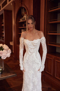 The Caprice Gown exudes royal elegance with its scalloped lace bodice, adorned with pearls and delicate lace sleeves that grace the hands. The unique scalloped detail extends to the hem and train, adding a touch of cascading beauty. Perfect for a regal and sophisticated look on any special occasion.