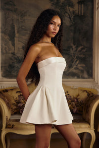 This elegant Strapless Opera Mini Dress in Pearl features a fold-over collar and a silicone gripper elastic that ensures a secure fit along the inner bodice. Designed with godets at the high hip and discreet built-in pockets, it offers both structure and functionality. The dress closes with an invisible zipper and hook-and-eye at the center back, enhanced by boning along the side seams and back for added support. 