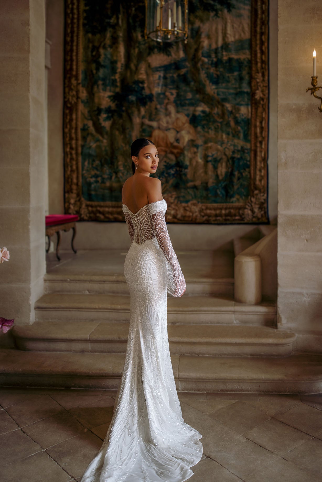 Effie is a luxurious fitted mermaid gown made of exclusive beaded lace. The off-shoulder neckline bares the collarbones adding seductiveness, the corset is decorated with sheer nude side pannels and long translucent lace sleeves look extravagant. The sheath skirt is embellished with thigh high slit and a Tulle overskirt is fastened on the waistline.