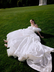Elevate your special day with the Fenny Gown. This ball-gown silhouette wedding dress features voluminous dropped straps and a hook-back closure. Crafted with luxurious taffeta, it exudes elegance and sophistication. Say "I do" in style with the Fenny Gown.