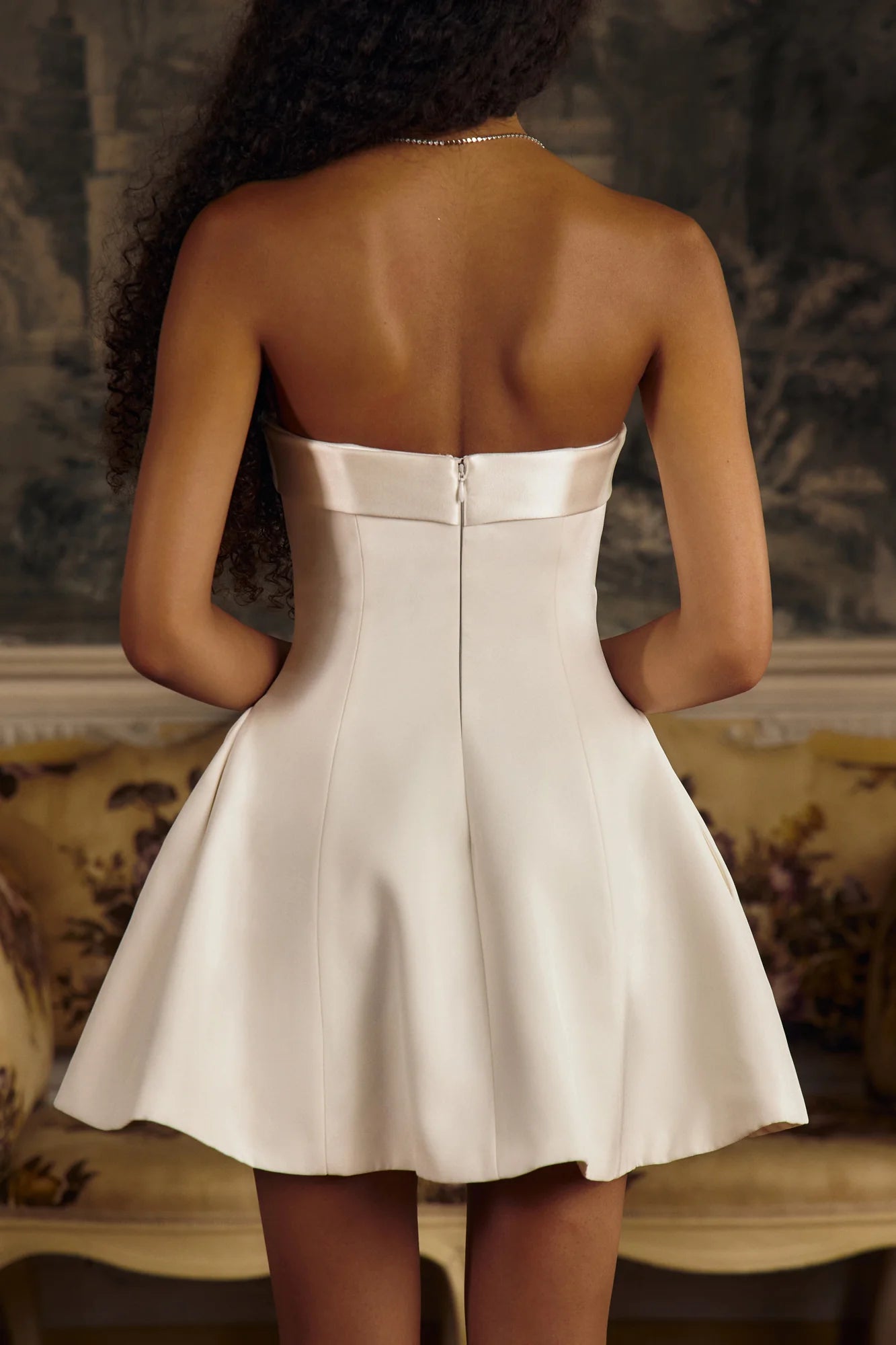 This elegant Strapless Opera Mini Dress in Pearl features a fold-over collar and a silicone gripper elastic that ensures a secure fit along the inner bodice. Designed with godets at the high hip and discreet built-in pockets, it offers both structure and functionality. The dress closes with an invisible zipper and hook-and-eye at the center back, enhanced by boning along the side seams and back for added support. 