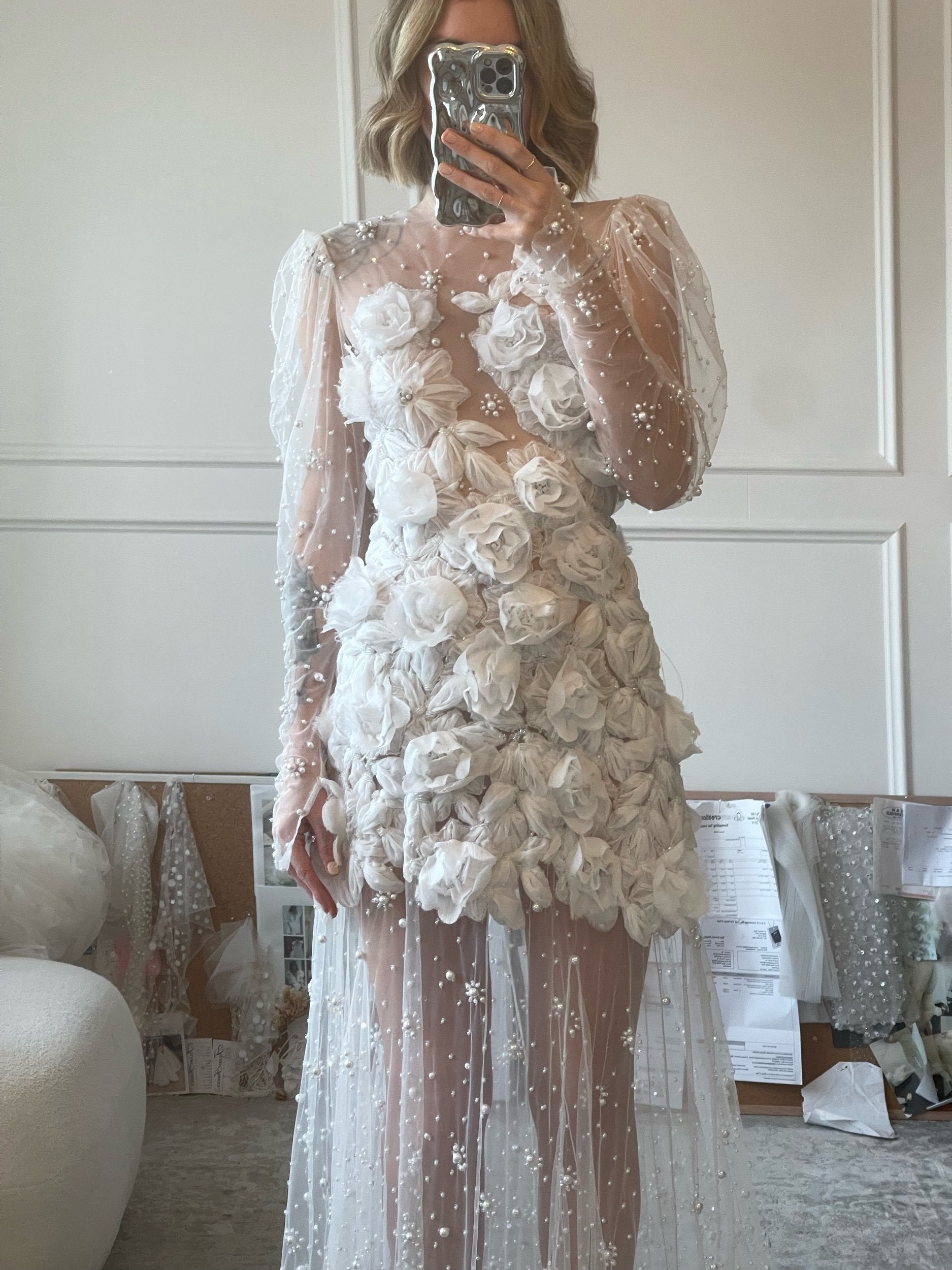 The Scarlett Dress is a dream come true for the romantic bride. Crafted from soft tulle, the bodice is adorned with delicate pearl beading and stunning 3D floral appliques, while the long sleeves and sheer godet skirt add a touch of whimsy and movement. Make a statement on your special day with this magical design.