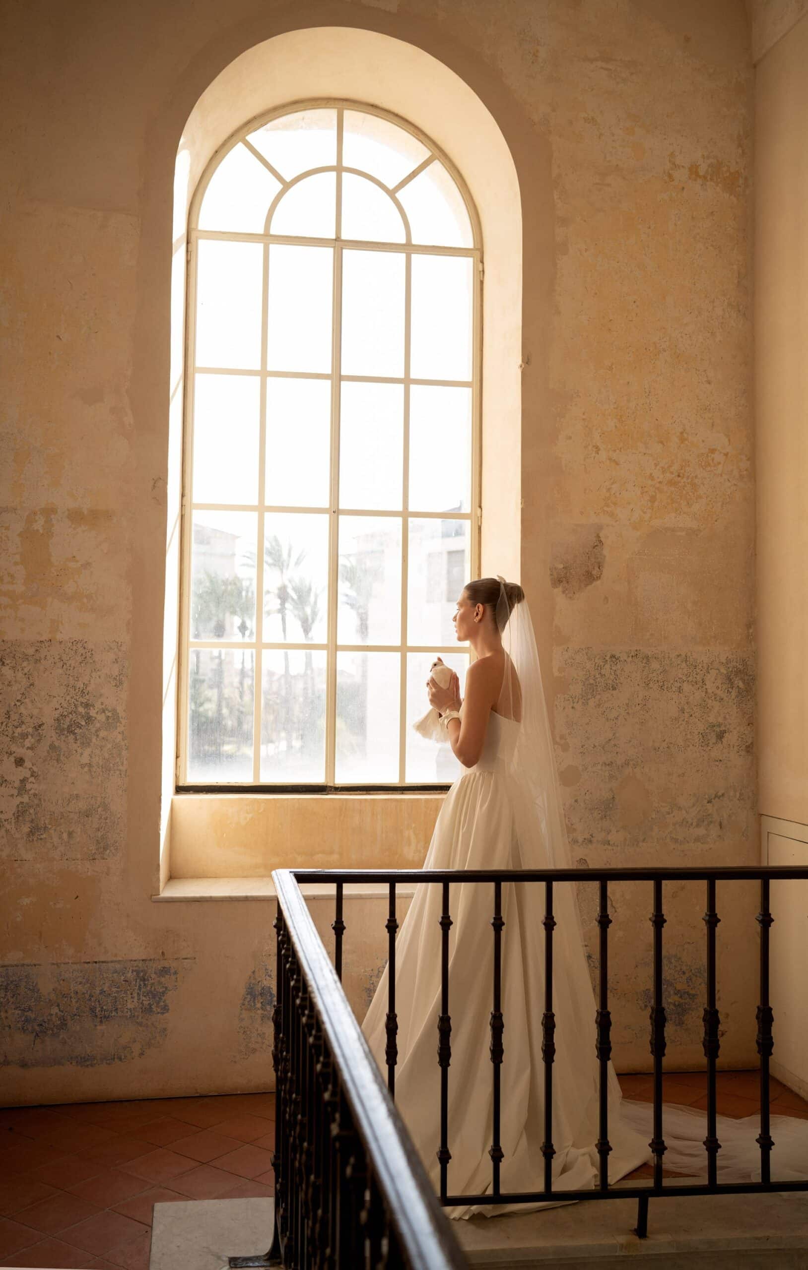 Elevate your special day with the Blue Gown. Made from luxurious Silk Mikado, it features a strapless sweetheart corset and basque waist for a flattering fit. The unique bow-shaped off-shoulder sleeves, coordinating gloves, and matching veil add a touch of elegance and sophistication. Create unforgettable memories in this stunning princess gown.