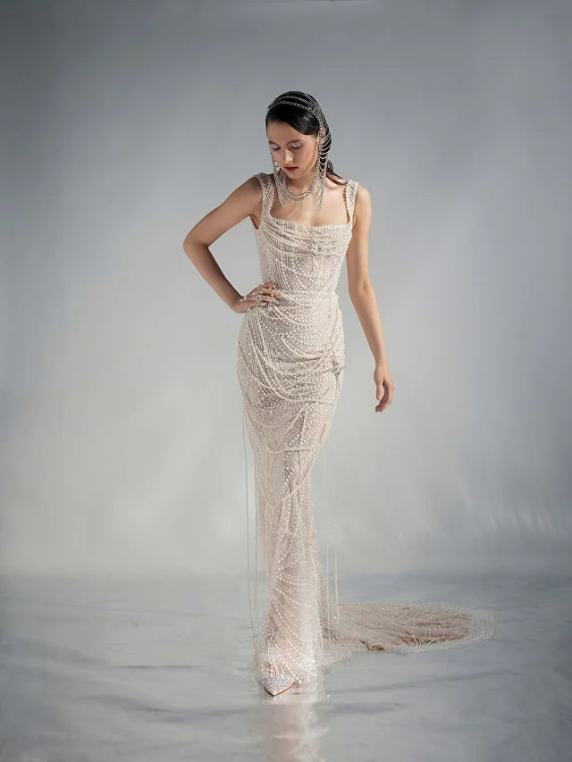Get ready to dazzle on your special day with the Versy Gown. The fitted silhouette is enhanced by a relief corset made of transparent mesh and lace, adorned with asymmetrical pearl threads. The whimsical silhouette skirt features scattered pearl threads and removable stars for a unique, ethereal touch. Say "I do" in style with the Versy Gown.