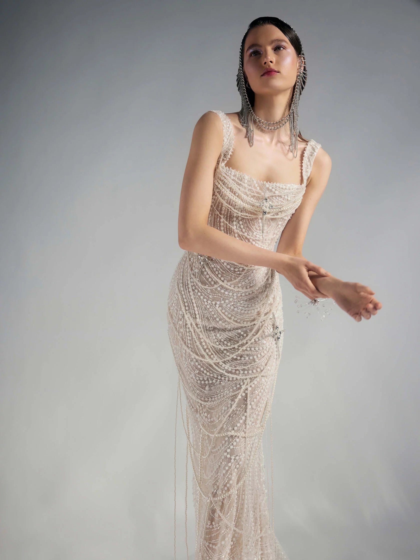 Get ready to dazzle on your special day with the Versy Gown. The fitted silhouette is enhanced by a relief corset made of transparent mesh and lace, adorned with asymmetrical pearl threads. The whimsical silhouette skirt features scattered pearl threads and removable stars for a unique, ethereal touch. Say "I do" in style with the Versy Gown.