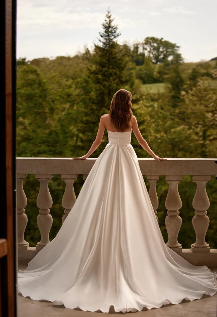 Elegant and luxurious, the Petal Gown is a beautiful option for the delicate and determined bride. The A-line silhouette is made of Mikado fabric, with a corset featuring a unique heart cutout and nude-colored mesh insert. The back of the corset is adorned with horizontal pleats and fastened with expander hooks. The full skirt, also in Mikado fabric, has a playful slit and diagonal pleating on the front panel.