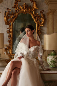 Introducing the Regina Gown, a light skin A-line dress that will make any bride the star of the wedding. The semi-sheer corset with a deep heart cutout and embroidered lace patterns adds a seductive touch, while the fluffy skirt and luxurious train create a stunning silhouette. Available in ivory.