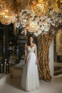 Elevate your special day with our Robe Mae. The elegant column silhouette features stunning beaded lace for a touch of glamour, while the off-shoulder sheer sleeves and deep v-neckline add a hint of romance. Complete the look with the delicate tulle skirt, for a dreamy and unforgettable bridal ensemble.