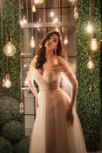 Elevate your special day with our Robe Mae. The elegant column silhouette features stunning beaded lace for a touch of glamour, while the off-shoulder sheer sleeves and deep v-neckline add a hint of romance. Complete the look with the delicate tulle skirt, for a dreamy and unforgettable bridal ensemble.