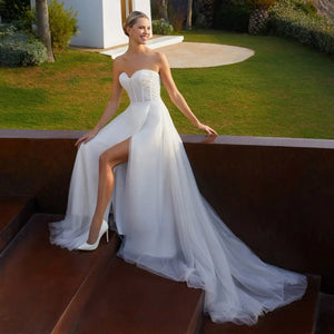 Robe Courtney is a stunning wedding dress that exudes sophistication and luxury. Crafted with simple yet elegant details such as a sleeveless silhouette, shiny A-line skirt, and beautiful side split, this dress highlights your figure without compromising comfort. Complete with a sweetheart neckline, pleats, lace belt, and backless design, you'll look like royalty on your special day.