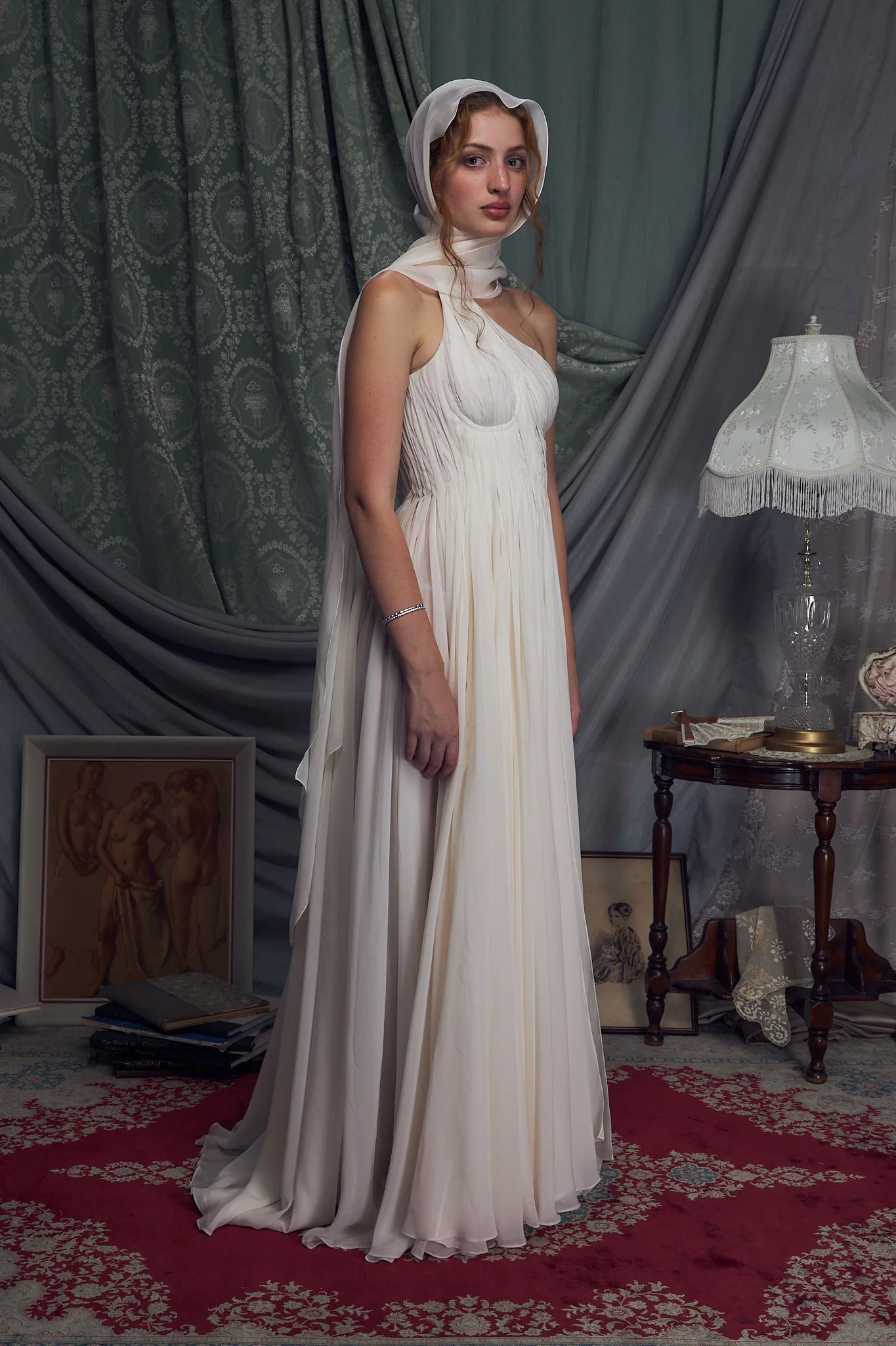The Hellenistic Gown features a graceful one-shoulder design crafted from delicate crinkle chiffon, offering both elegance and movement. Built with underwire cups and a power mesh torso lining, it provides structured support and a flattering fit. An attached scarf adds a touch of sophistication, while the high slit accentuates leg lines for a striking silhouette. The gown secures with an invisible zipper and hook-and-eye closure at the center back, ensuring a seamless finish. 