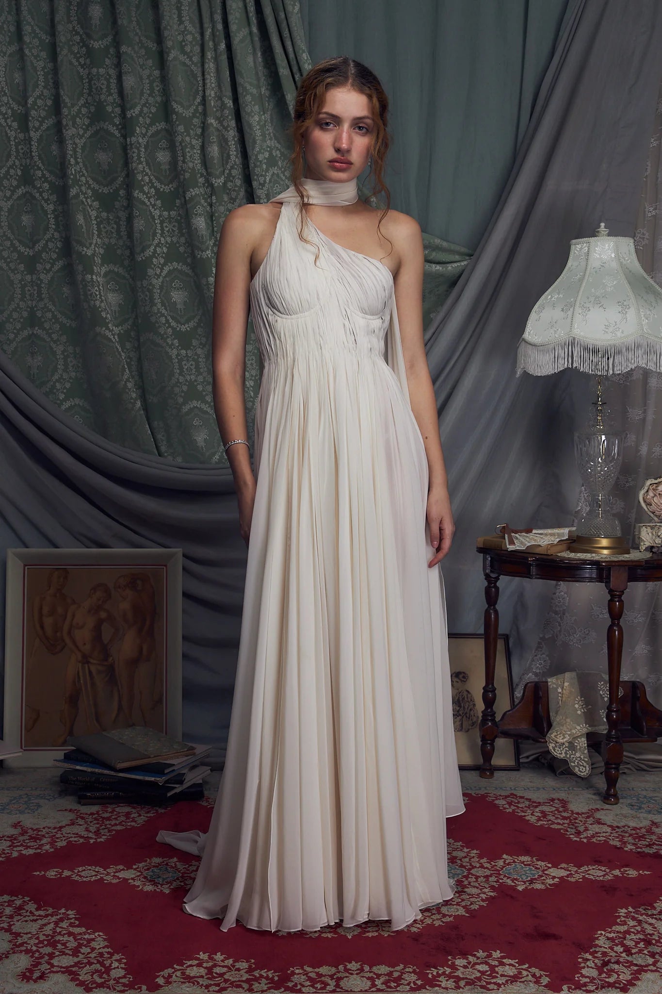 The Hellenistic Gown features a graceful one-shoulder design crafted from delicate crinkle chiffon, offering both elegance and movement. Built with underwire cups and a power mesh torso lining, it provides structured support and a flattering fit. An attached scarf adds a touch of sophistication, while the high slit accentuates leg lines for a striking silhouette. The gown secures with an invisible zipper and hook-and-eye closure at the center back, ensuring a seamless finish. 