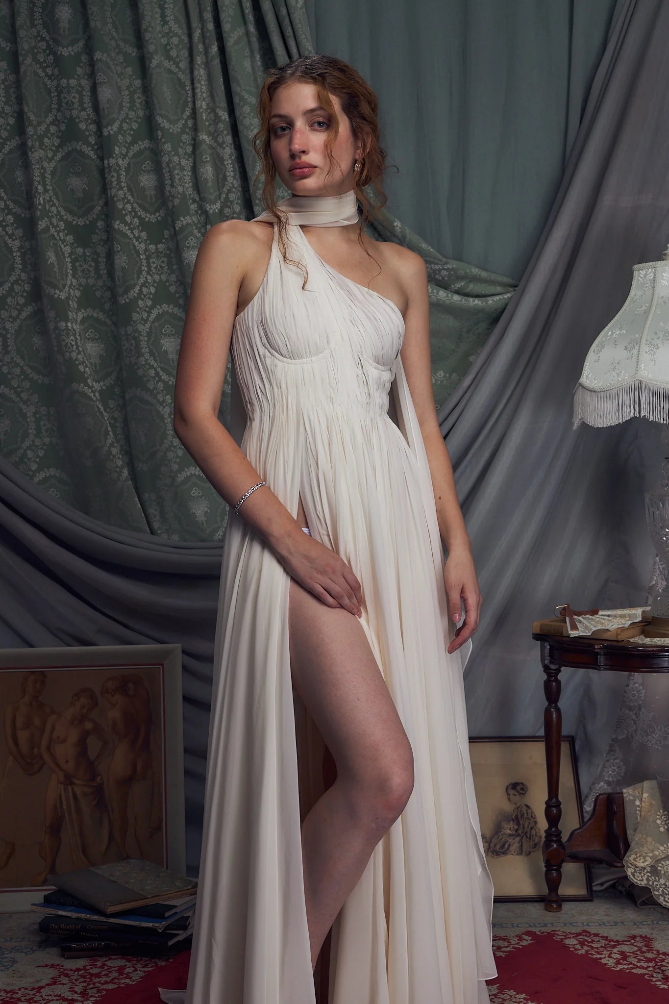 The Hellenistic Gown features a graceful one-shoulder design crafted from delicate crinkle chiffon, offering both elegance and movement. Built with underwire cups and a power mesh torso lining, it provides structured support and a flattering fit. An attached scarf adds a touch of sophistication, while the high slit accentuates leg lines for a striking silhouette. The gown secures with an invisible zipper and hook-and-eye closure at the center back, ensuring a seamless finish. 