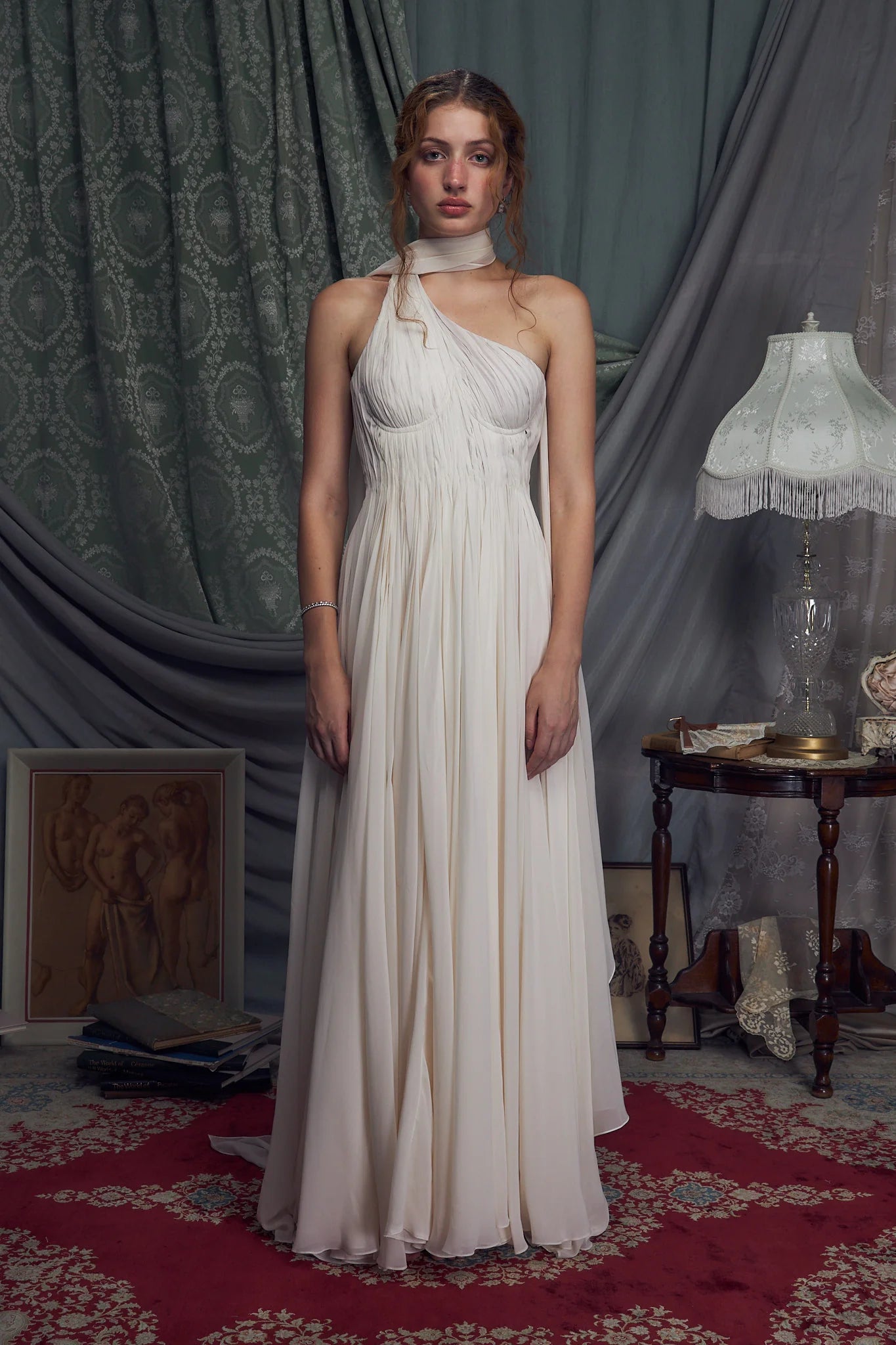 The Hellenistic Gown features a graceful one-shoulder design crafted from delicate crinkle chiffon, offering both elegance and movement. Built with underwire cups and a power mesh torso lining, it provides structured support and a flattering fit. An attached scarf adds a touch of sophistication, while the high slit accentuates leg lines for a striking silhouette. The gown secures with an invisible zipper and hook-and-eye closure at the center back, ensuring a seamless finish. 